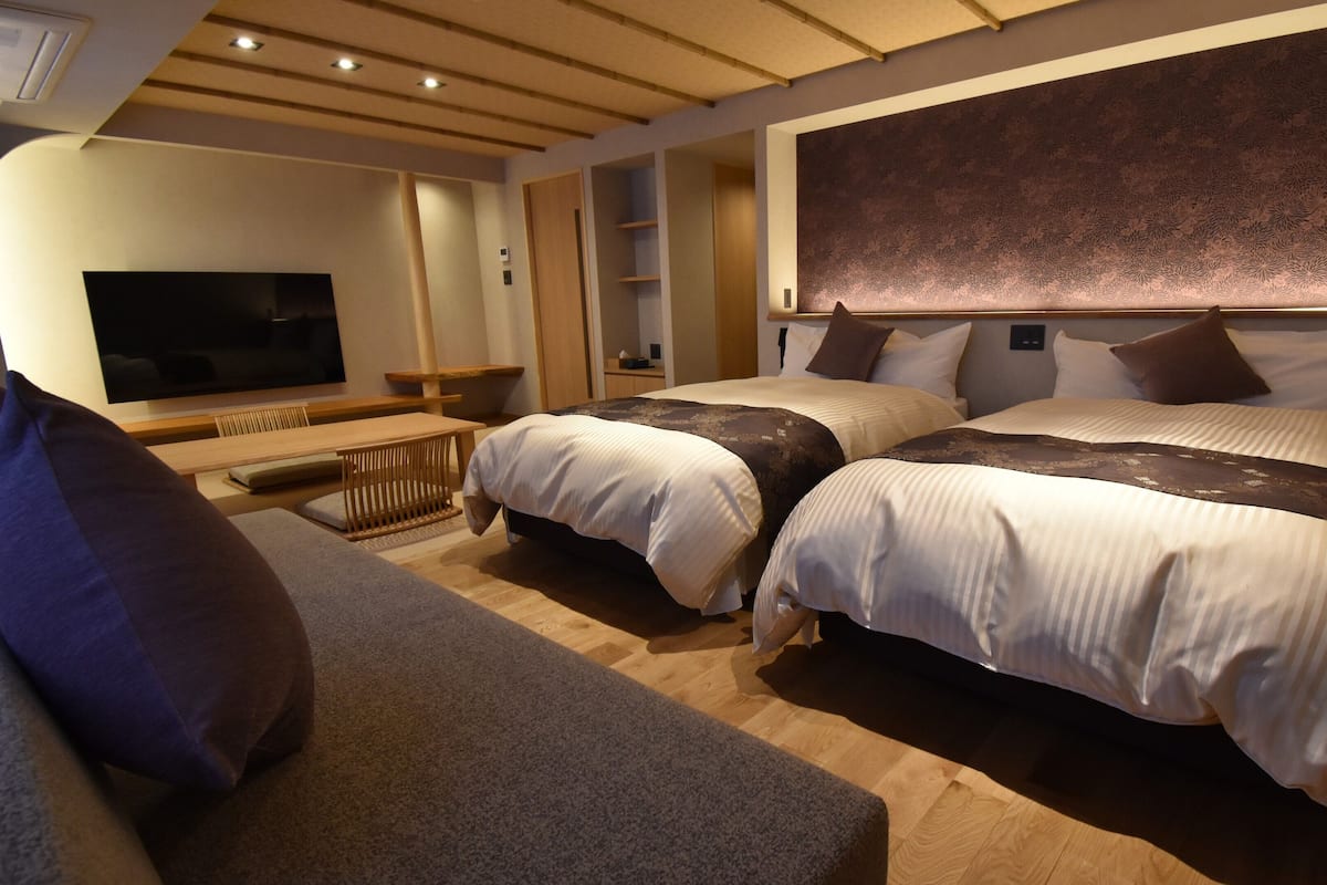 A hotel room with two beds, a TV, a sofa, and a desk.