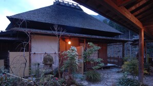 Una casa tradicional japonesa con techo de paja, un porche de madera y un sendero de piedra que lleva a la entrada.