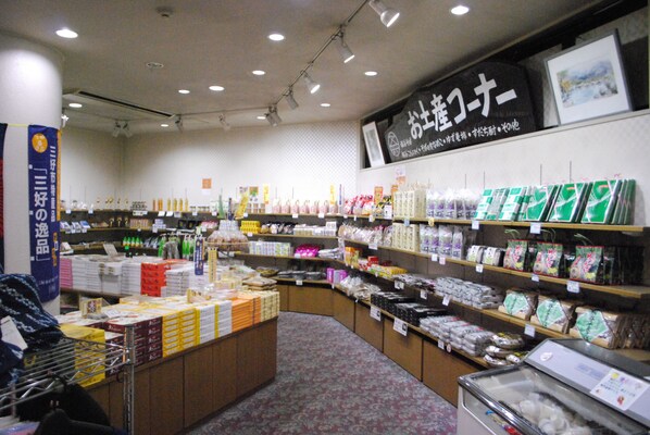 Interior de una tienda con estantes llenos de productos envasados, un mostrador de exhibición con cajas y un letrero con texto en japonés.