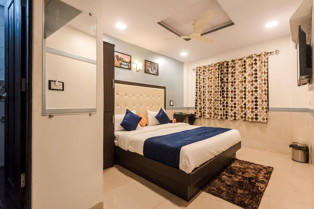 A hotel room with a bed, a nightstand, a ceiling fan, and a window with patterned curtains.
