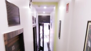 A hallway with a black and white tiled floor, a vent on the left wall, and a door at the end. - Hotel Aksa (Mumbai)