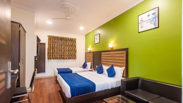 A hotel room with two beds, a sofa, a glass coffee table, and a green accent wall. - Hotel Aksa (Mumbai)