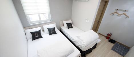 Une chambre d’hôtel de taille réduite, équipée de deux lits, d’une fenêtre, d’un climatiseur, d’une porte et d’un extincteur.