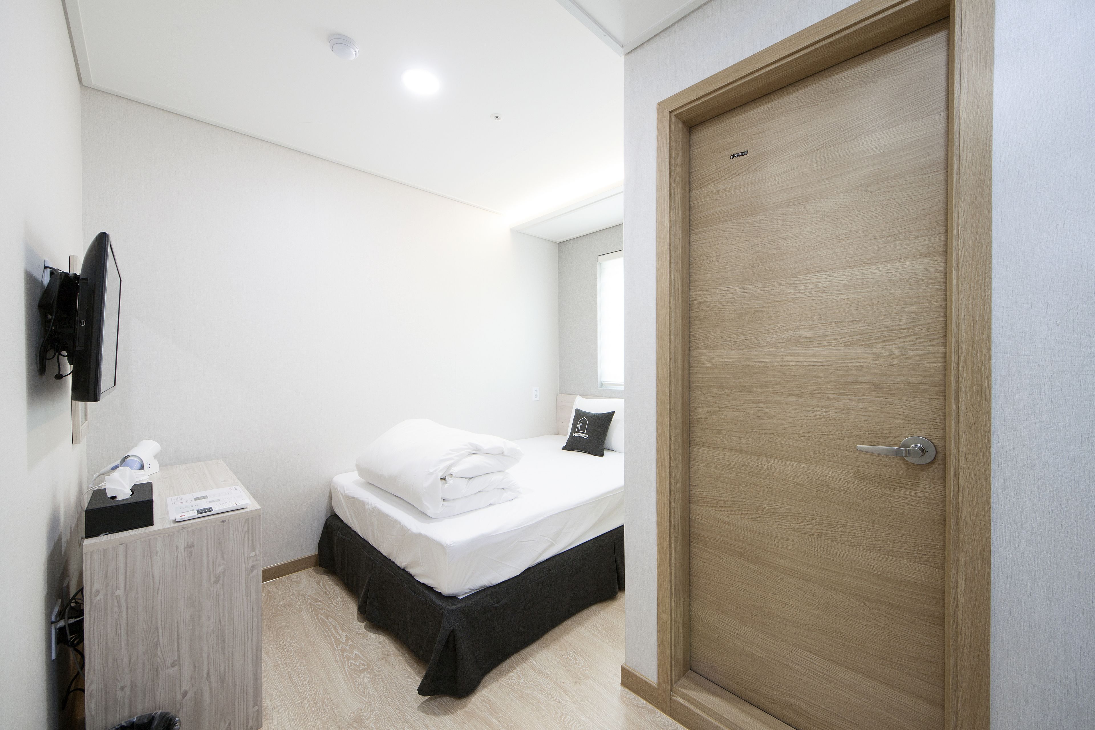 Ein Schlafzimmer mit einem Bett, einer Holztür, einem Nachttisch und einem an der Wand montierten Fernseher.