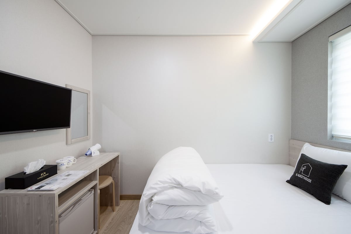 Habitación de hotel con cama, escritorio, televisor de pantalla plana, una silla y ventana con persianas.