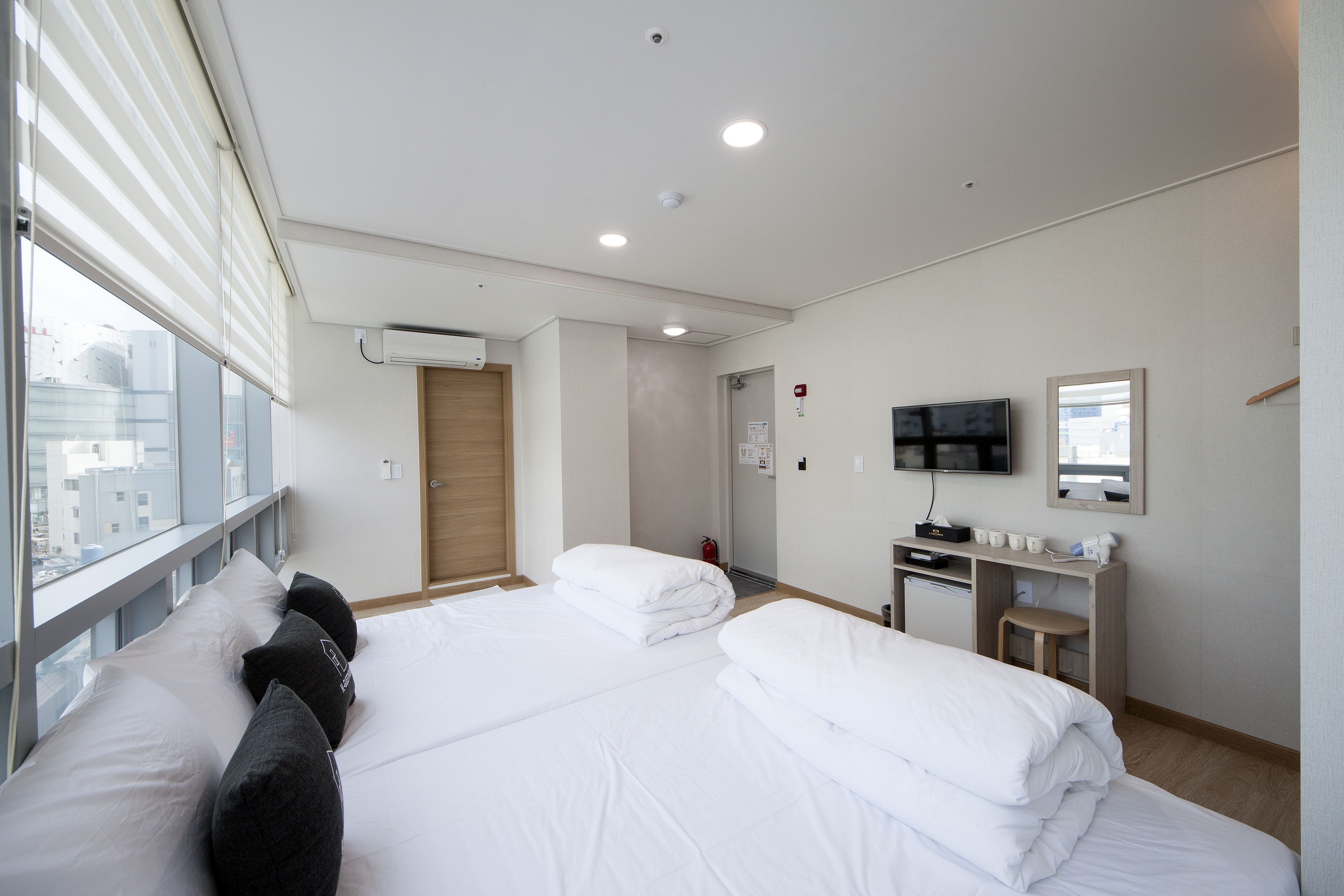 Une chambre d’hôtel avec deux lits, un bureau, une télévision et une fenêtre avec des stores.