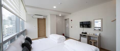A hotel room with two beds, a desk, a TV, and a window with blinds.