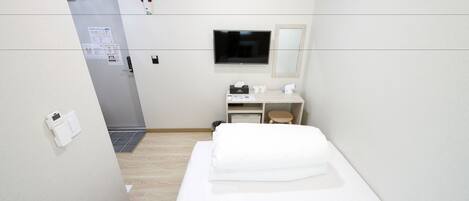 Camera d'albergo con un letto, una scrivania con una sedia, una televisione e un piccolo sgabello.