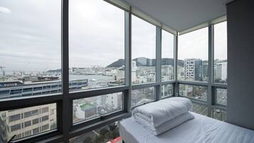 A hotel room with a large window offering a city view, a bed with white linens, and a view of a bridge and buildings.