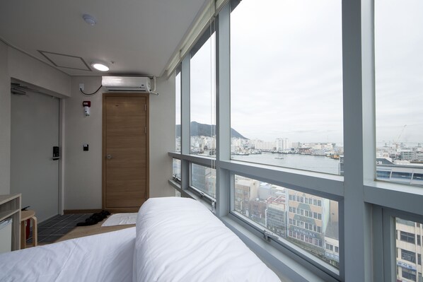 A hotel room with a bed, a desk, a chair, a window with a city view, and a door. - K-Guesthouse Premium Nampo 1 (Busan)