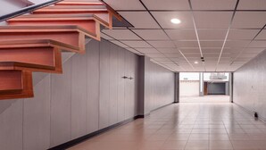 Un pasillo con una escalera de madera, piso de baldosas e iluminación empotrada en el techo.