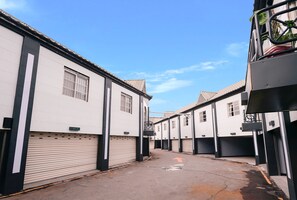 A narrow street with white buildings, closed garage doors, and a clear sky. - Cantaloupe Motel (Taoyuan City)