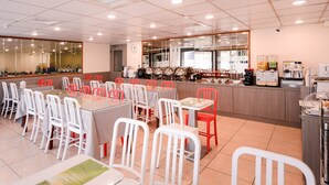 Un comedor con varias mesas y sillas, una encimera de cocina con electrodomésticos y un espejo grande en la pared.
