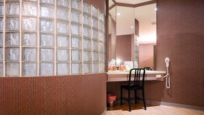 Un baño con pared de bloques de vidrio, un espejo, un lavabo, una silla y un teléfono.