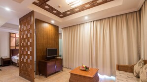 Une chambre d’hôtel équipée d’une télévision, d’une cloison en bois, d’un canapé en osier et d’une grande fenêtre avec des rideaux.