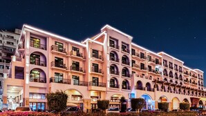 Un hôtel à plusieurs étages, doté de balcons, de fenêtres en arc de cercle et d’une façade bien éclairée.