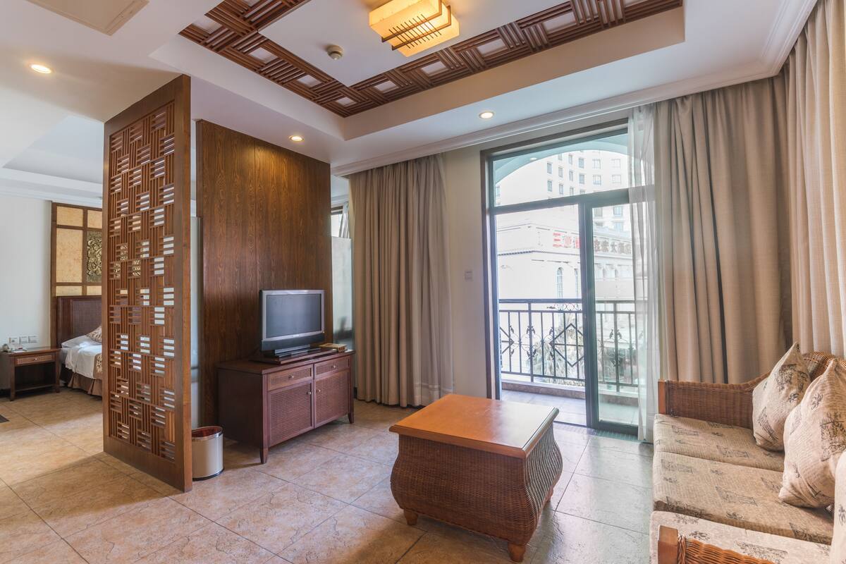 Une chambre d’hôtel équipée d’une télévision, d’un canapé, d’une cloison en bois et d’un balcon avec des rideaux.