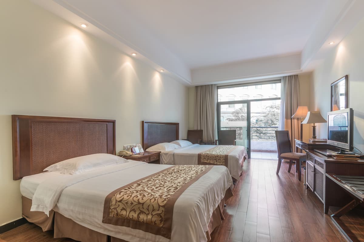 Une chambre d’hôtel avec deux lits, un bureau avec une télévision et une vue sur l’extérieur grâce à une grande fenêtre.