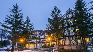 A large, historic building with a prominent clock tower, surrounded by tall trees and a snow-covered ground. - Rosen Heim HAKUBA (Hakuba)