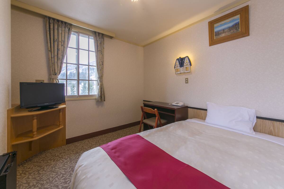 A hotel room with a bed, a desk, a chair, a television, and a window with curtains.