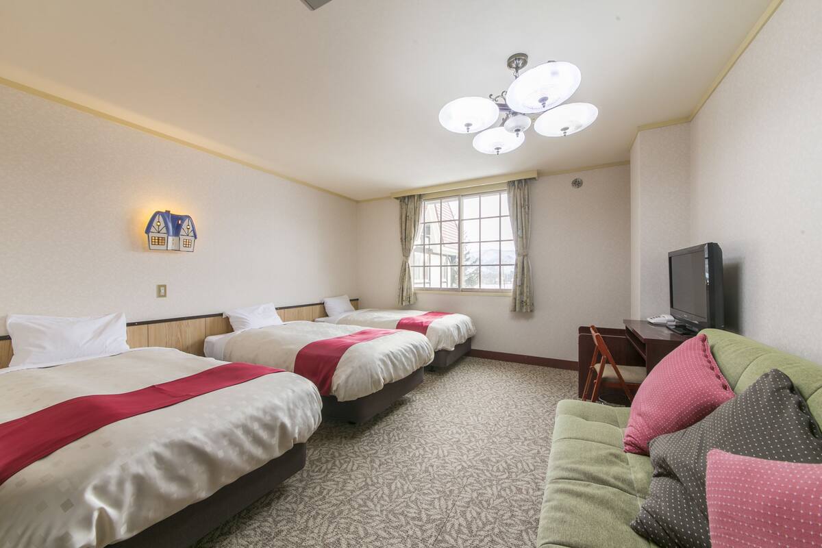 A hotel room with three beds, a television, a desk, and a window with curtains.