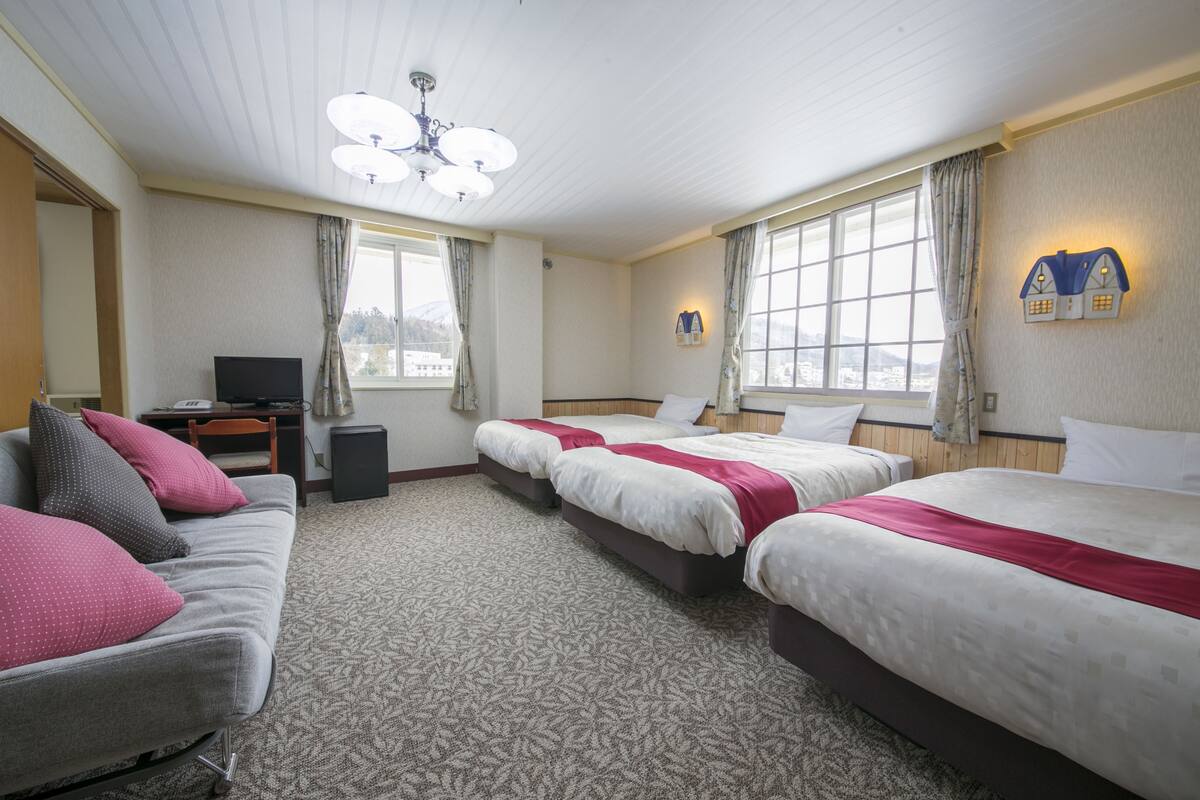 A hotel room with two beds, a sofa, a television, and a desk.