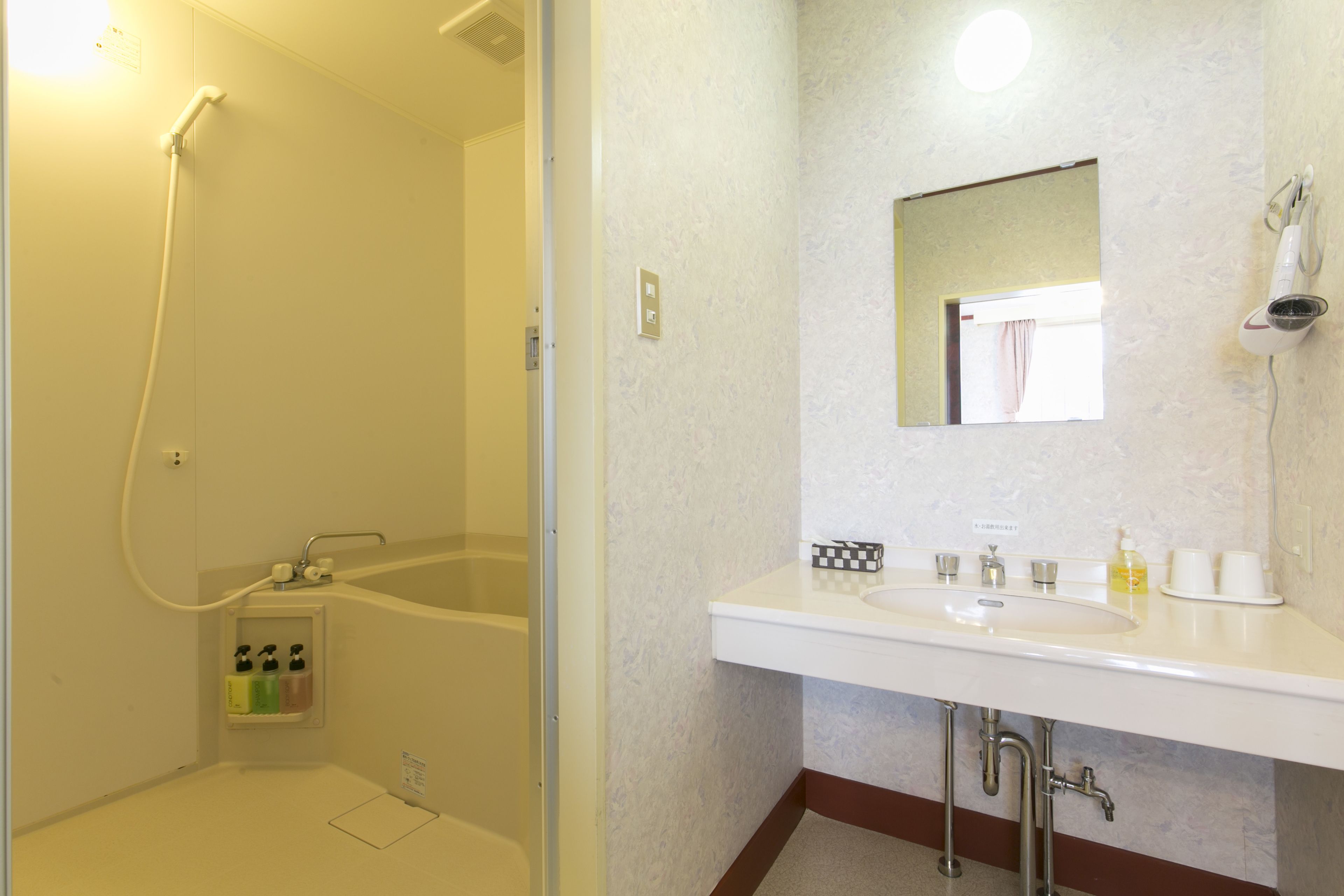 A bathroom with a bathtub, a sink with a mirror above it, and a hairdryer mounted on the wall.