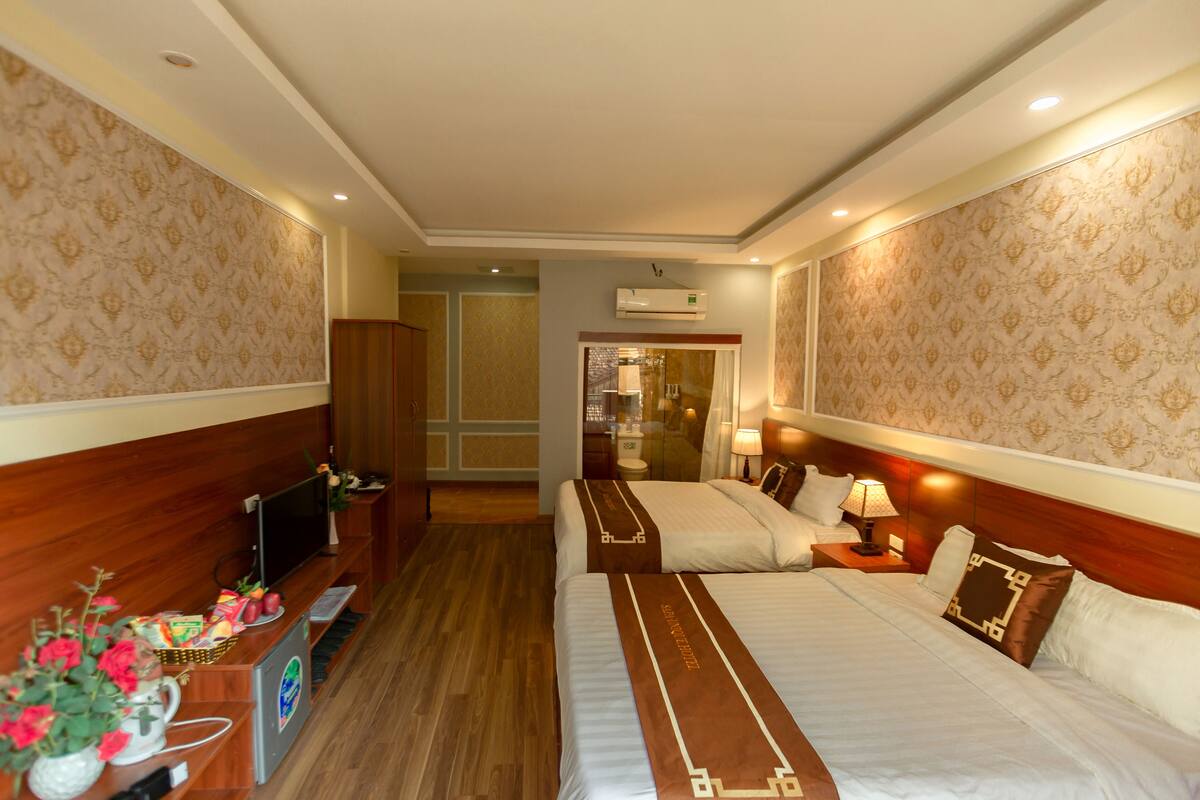 Ein Hotelzimmer mit zwei Betten, einem Fernseher, einem Schreibtisch mit Computer und einem durch eine Glastür einsehbaren Badezimmer.
