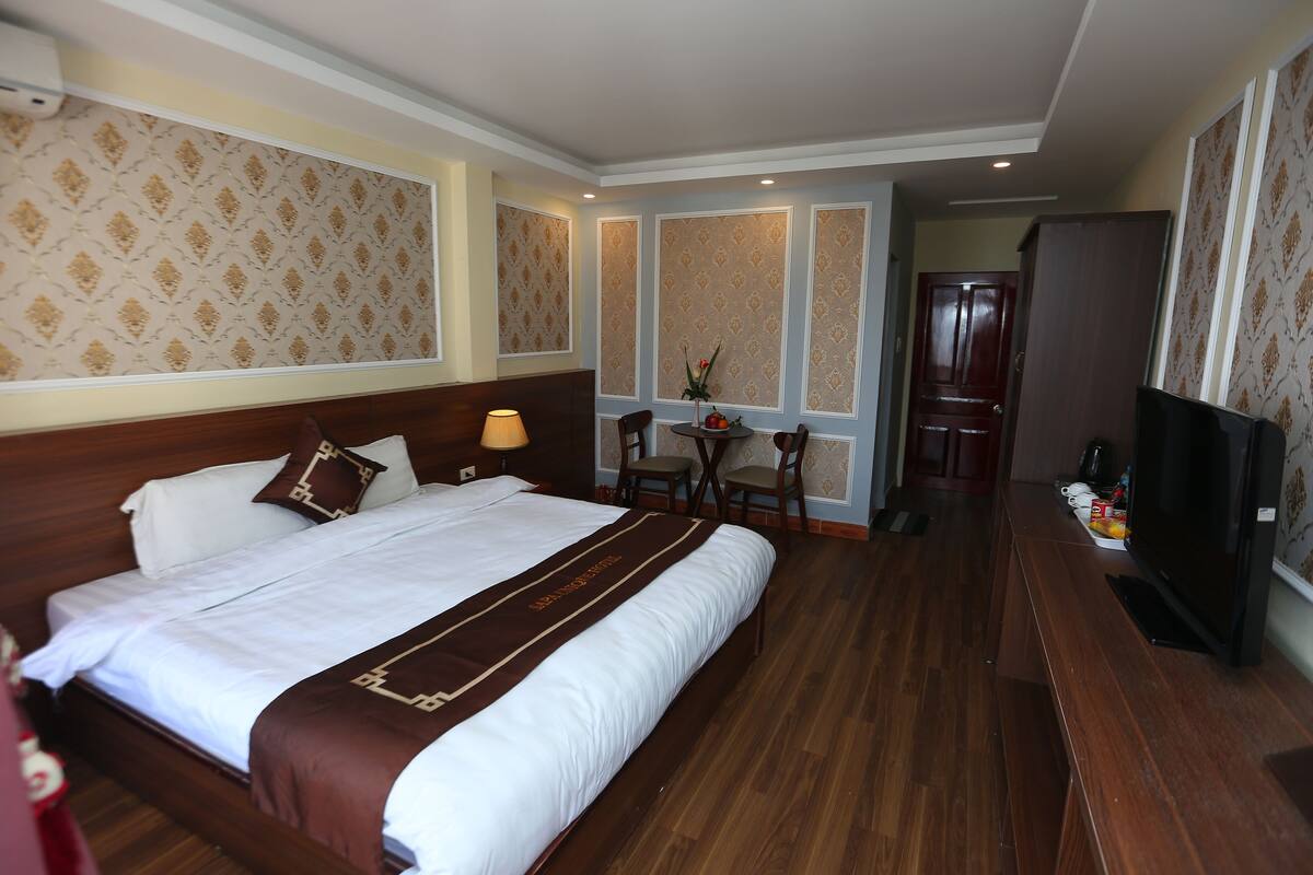 Ein Hotelzimmer mit einem großen Bett, einem Schreibtisch mit Stuhl, einem Fernseher und einem Kleiderschrank.