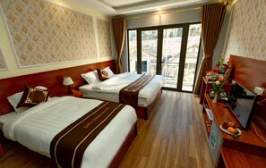 A hotel room with two beds, a wooden headboard, a desk with a TV, and a view of a building through a large window. - Sapa Unique Hotel (Sa Pa)