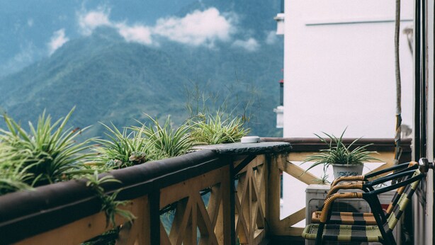 Un balcon agrémenté de plantes en pot, une chaise en osier et une vue sur les montagnes.