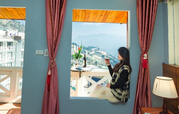A room with a large window, a table with a bottle and a glass, and a lamp. - Sapa Unique Hotel (Sa Pa)
