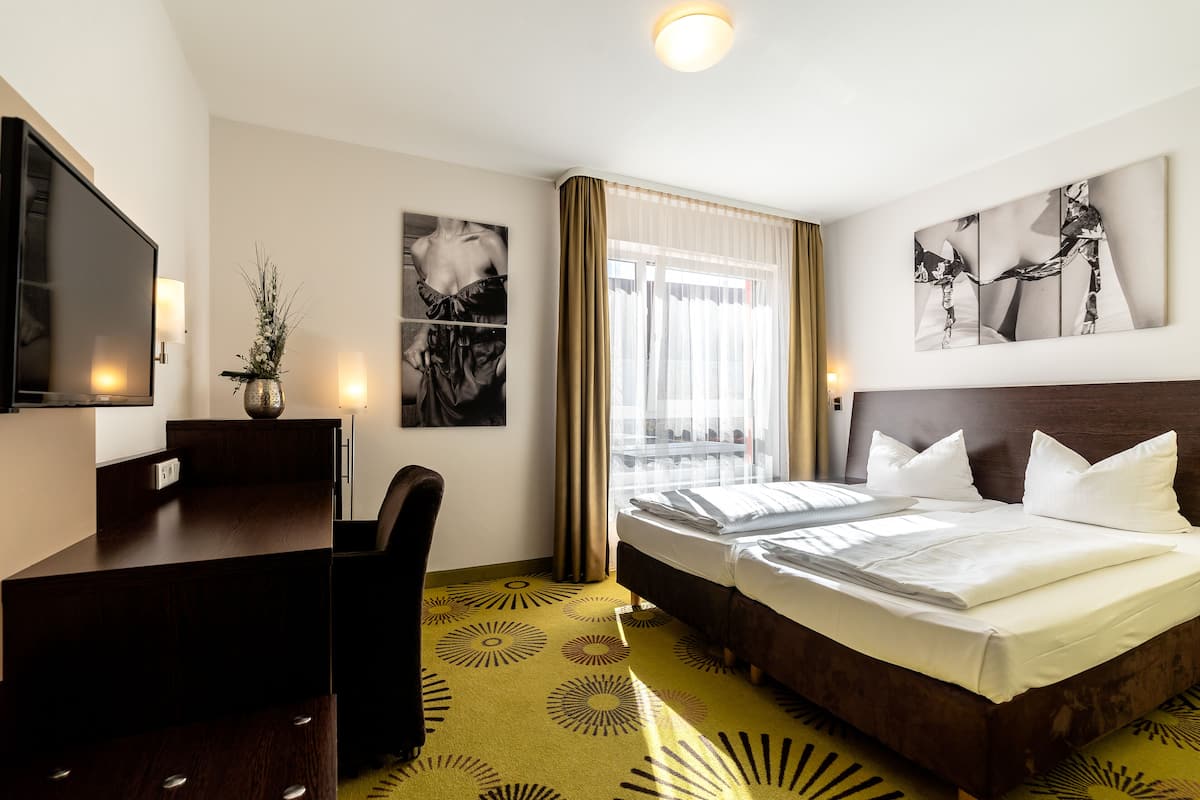 A hotel room with a bed, a desk, a television, and artwork on the walls.