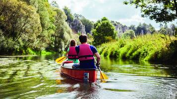 Una pareja en un canoa roja en un río tranquilo rodeado de vegetación exuberante y acantilados rocosos.