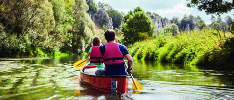 Un couple dans un canoë rouge, sur une rivière paisible, entouré d’une végétation luxuriante et de falaises rocheuses.