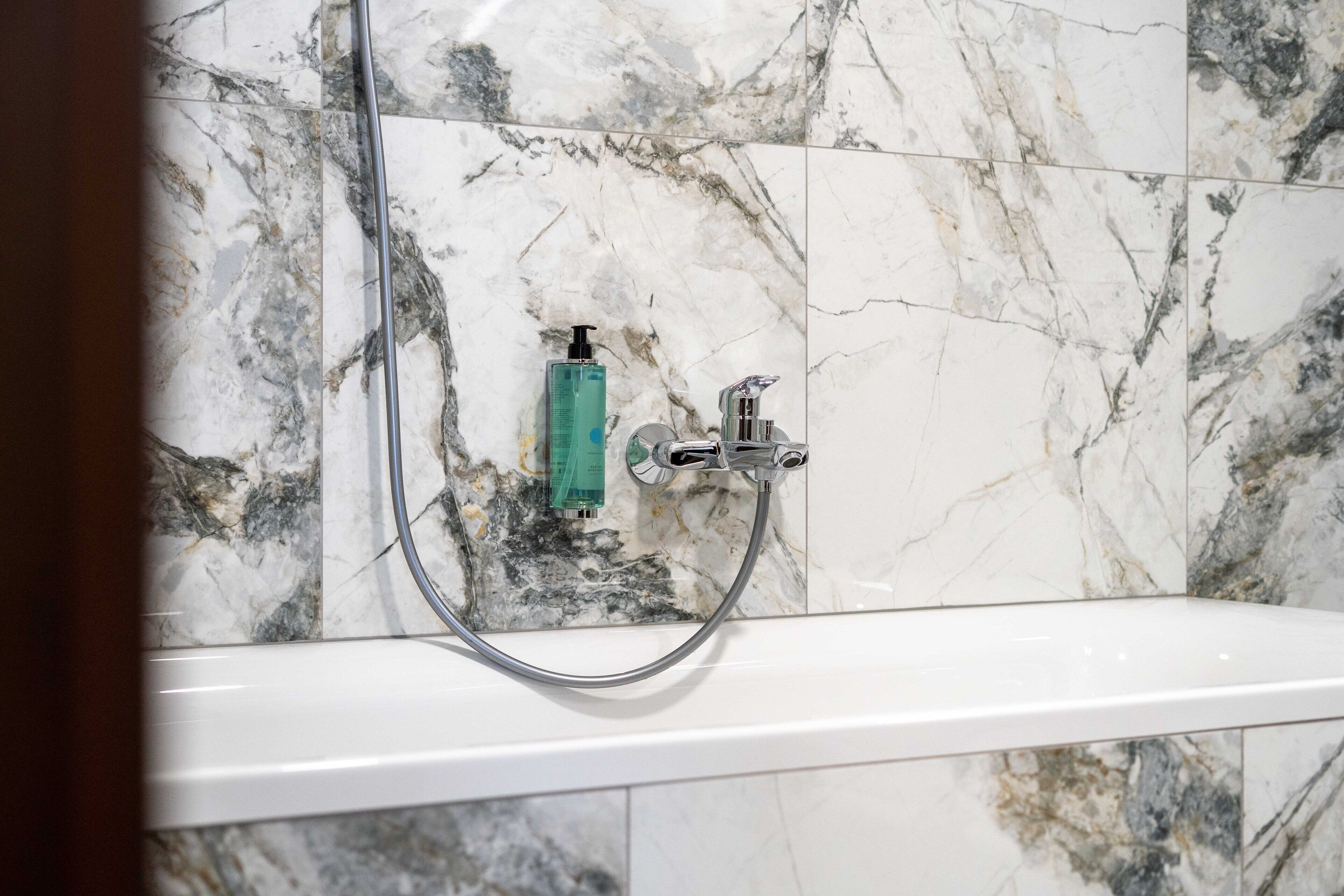 A bathroom with a white bathtub, a handheld showerhead, and a bottle of shampoo on the wall.