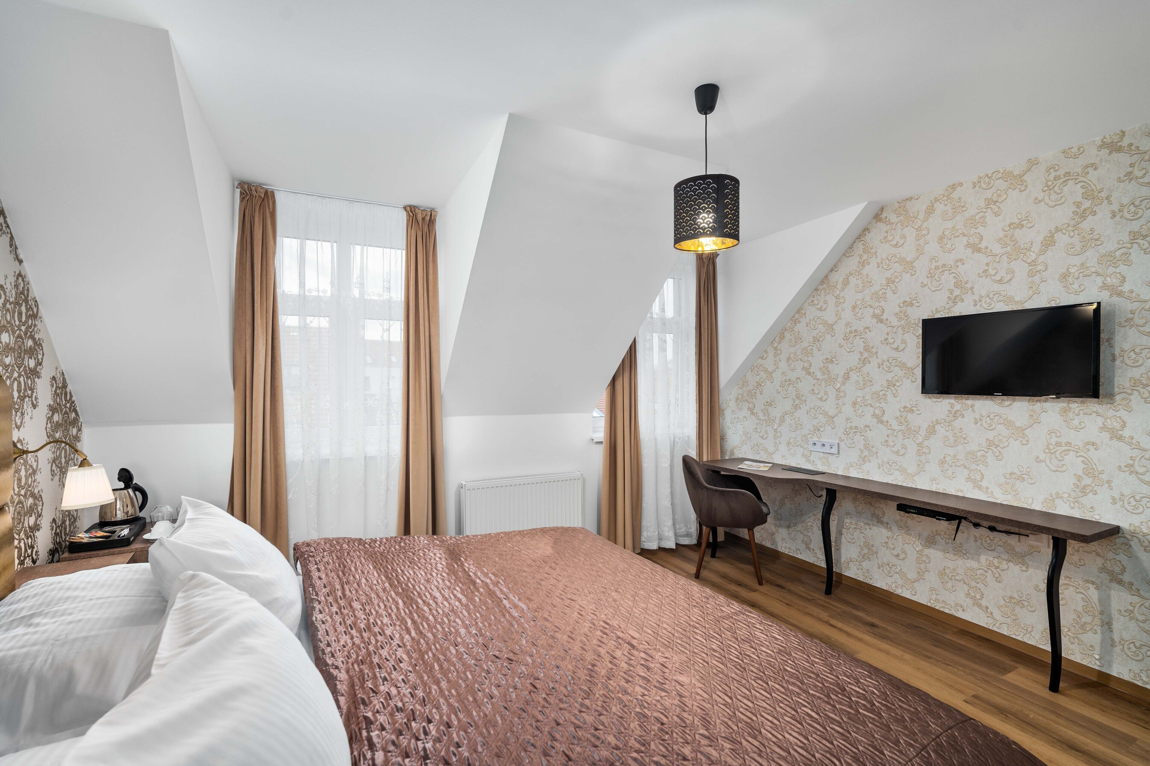 A hotel room with a bed, a desk, a chair, a television, and a window with curtains.