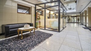 Un vestíbulo moderno con un panel de vidrio, un sofá de cuero negro, una mesa dorada y una alfombra decorativa.
