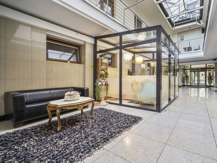 Eine moderne Lobby mit Glastrennwand, einer schwarzen Ledersofa, einem Goldtisch und einem dekorativen Teppich.