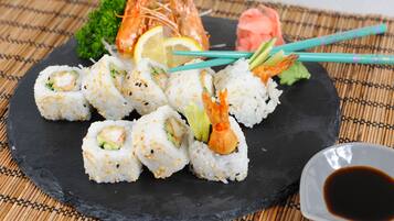 A black slate plate with sushi rolls, shrimp, lemon, and a small dish of soy sauce.