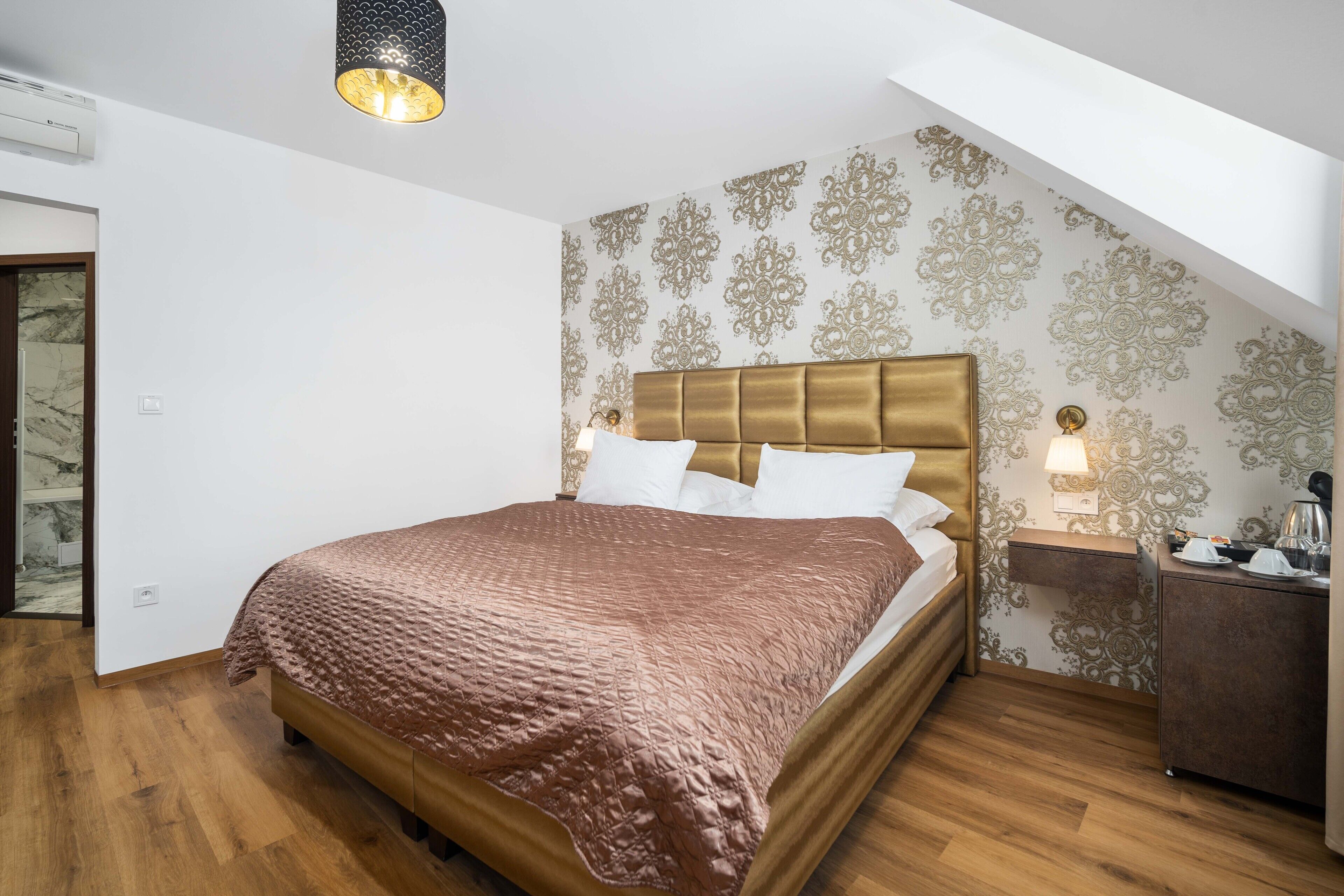 Une chambre à coucher avec un grand lit, une table de chevet, une lampe et un mur recouvert d’un papier peint à motifs.
