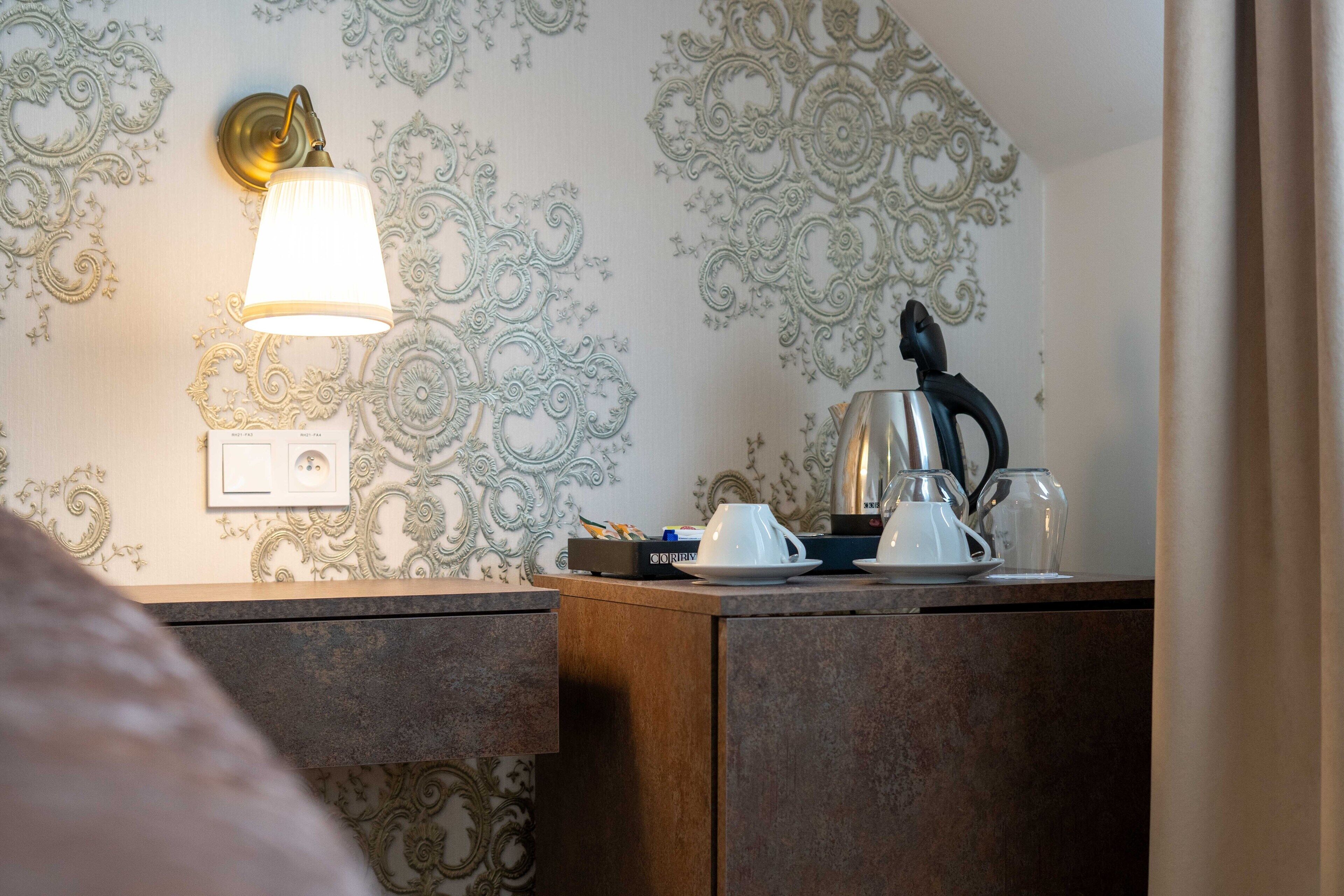 A hotel room with a decorative wall, a bedside table with a lamp, and a kettle.
