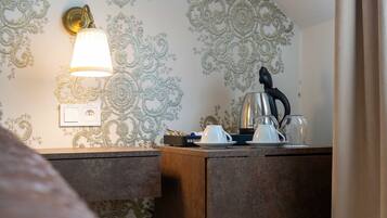 A hotel room with a decorative wall, a bedside table with a lamp, and a kettle.