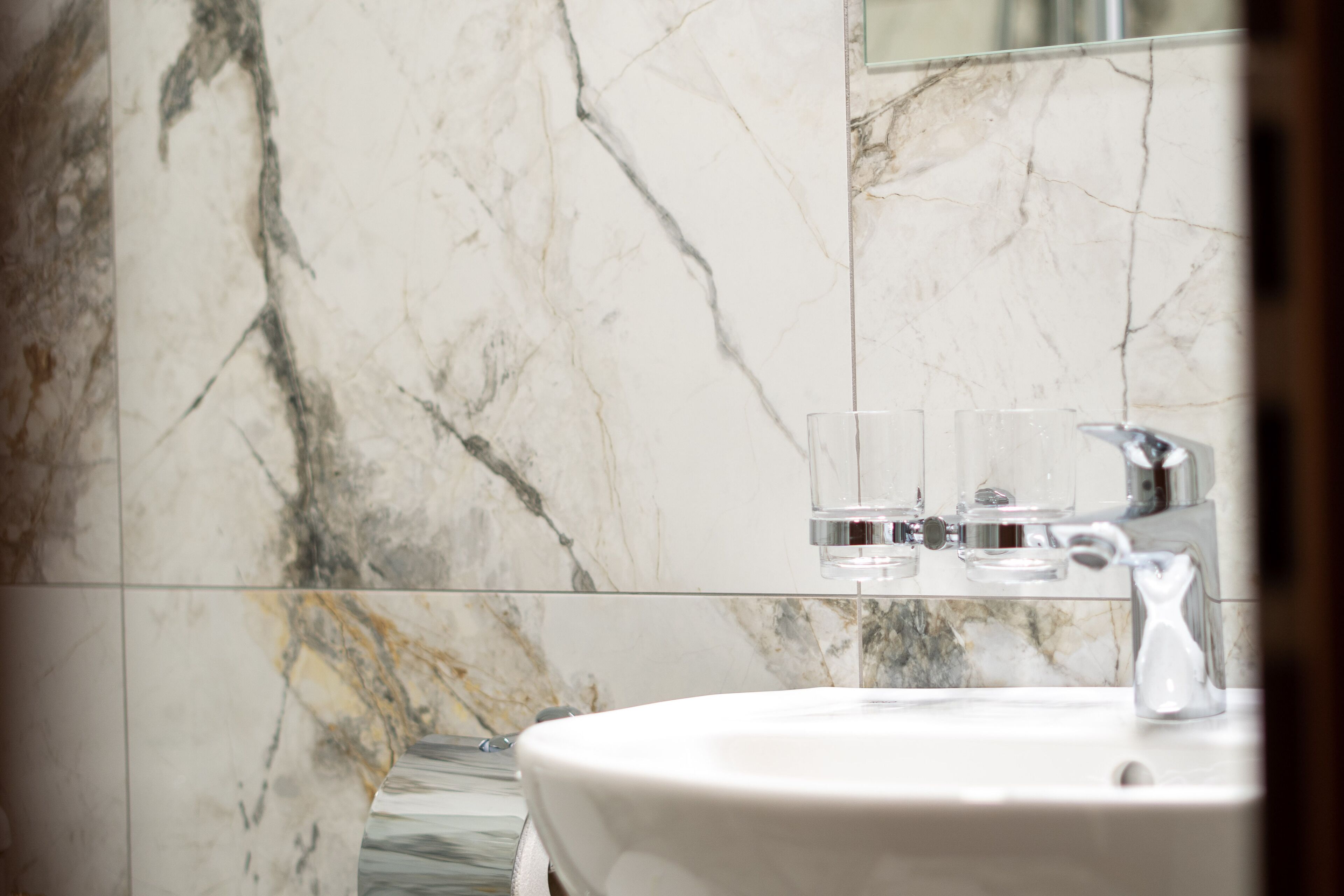 A bathroom with a marble wall, a sink, and a glass of water.