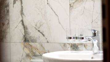 A bathroom with a marble wall, a sink, and a glass of water.