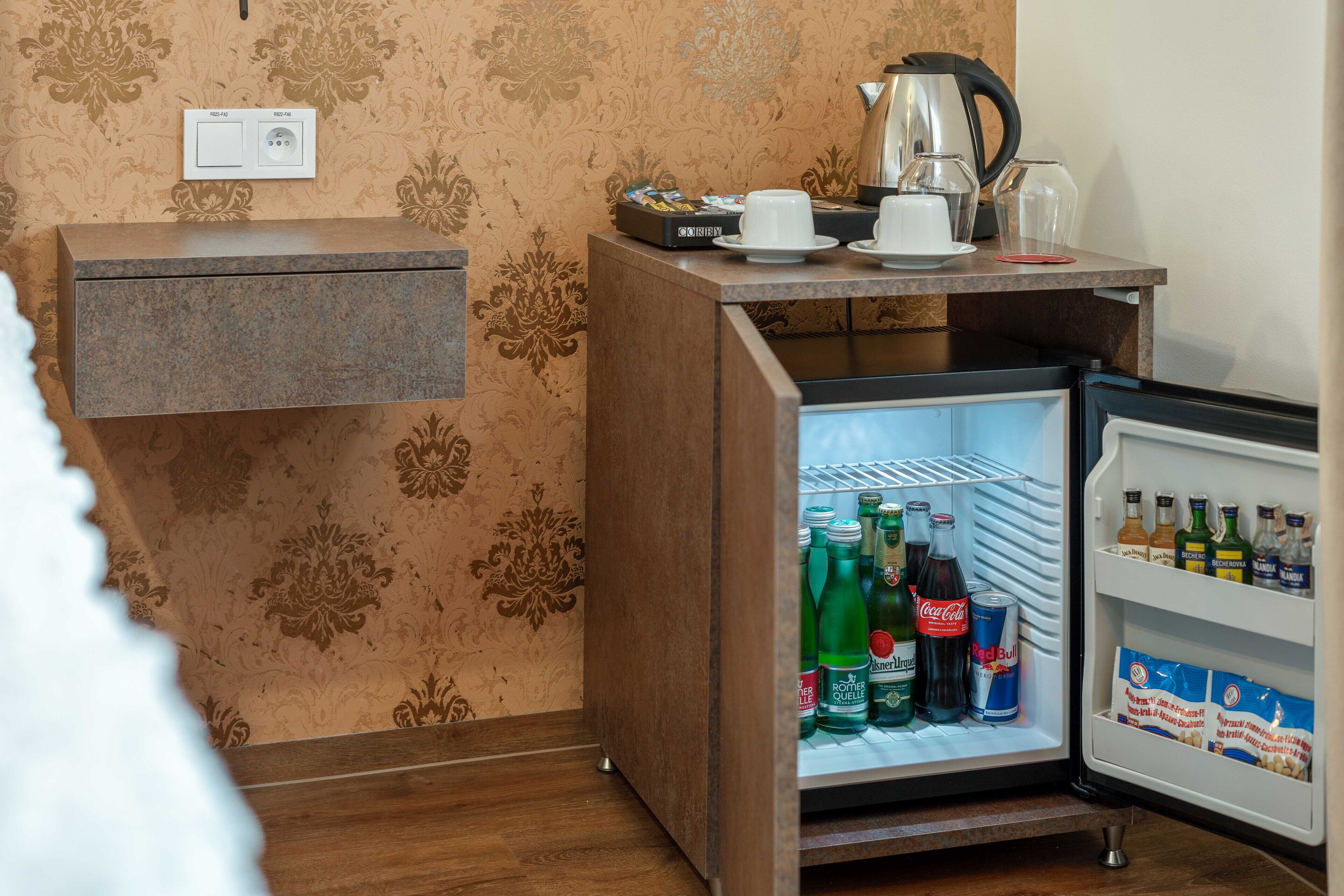 Una kitchenette compacta con un refrigerador lleno de bebidas, una cafetera y un hervidor.