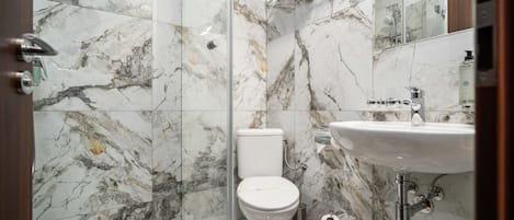 Un baño con piso de mármol, inodoro, lavamanos y zona de ducha.