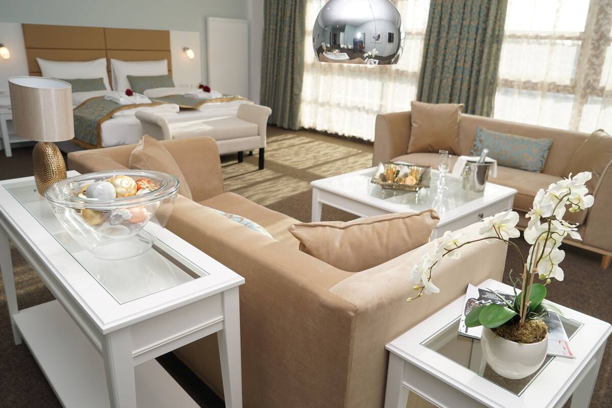 Ein modernes Hotelzimmer mit einem großen Bett, zwei Sofas, einem Esstisch und einem Topf mit einer Orchidee.