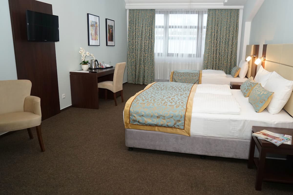 Ein Hotelzimmer mit Bett, Nachttischen, Schreibtisch, Stuhl, Fernseher und einem Fenster mit Vorhängen.