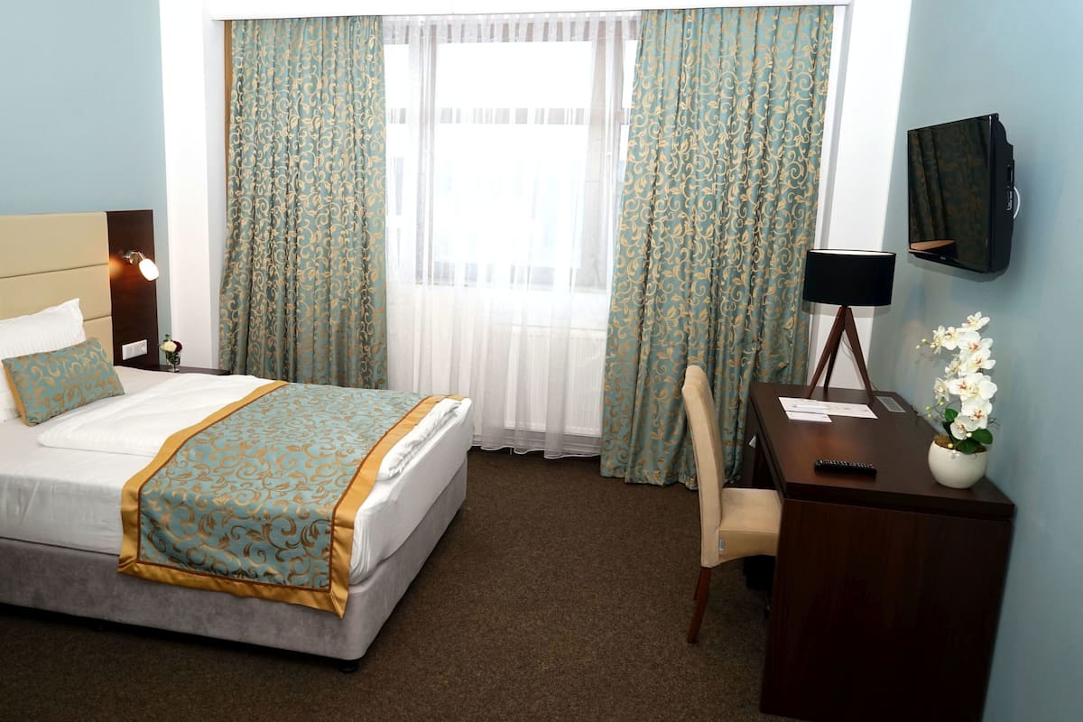 Ein Hotelzimmer mit Bett, Nachttisch, Stuhl, Schreibtisch, Fernseher und Vorhängen.